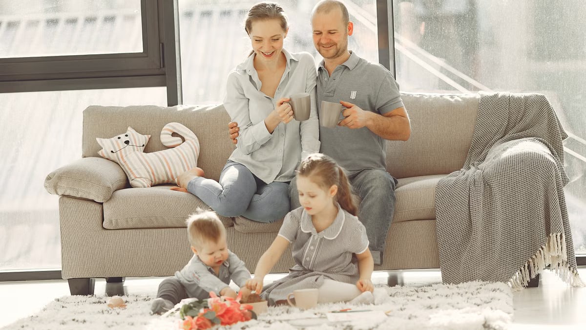 Cheerful family wearing casual clothes sitting in living room while playing and drinking tea during weekend at home in morning